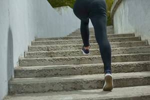 Girl athlete is jogging in morning outside, in the city, on stairs surrounded by green trees. Active healthy lifestyle. Sport and recreation concept. photo