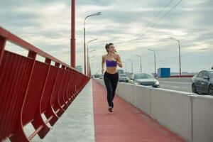 Girl athlete is jogging in the morning outside, in the city, on modern bridge crossing river. Active healthy lifestyle. Sport and recreation concept. photo