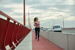 Girl athlete is jogging in the morning outside, in the city, on modern bridge crossing river. Active healthy lifestyle. Sport and recreation concept. photo
