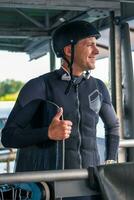 Cheerful wakeboarder in wetsuit and helmet standing with board on start dock before training photo