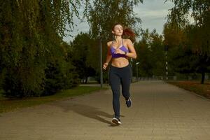 Girl athlete is jogging in morning outside, in the city, on a park path surrounded by trees. Active healthy lifestyle. Sport and recreation concept. photo