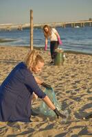 joven voluntarios en negro guantes son caminando con basura pantalones a lo largo un sucio playa de el río y limpieza arriba basura. personas y ecología. de cerca. foto