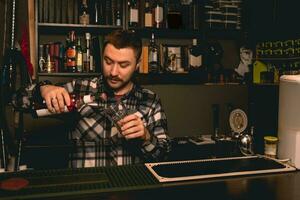 Bartender preparing cocktail behind bar counter, pouring berry liquor into glass photo