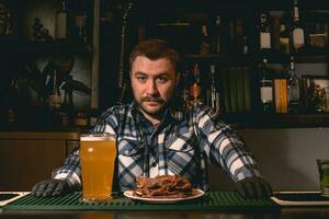 barman en pie detrás bar mostrador en pub con vaso de cerveza y plato de meriendas foto