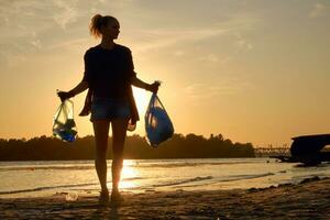 Young girl in black gloves is walking with garbage bags along a dirty beach of the river and cleaning up trash. People and ecology. Close-up. photo