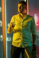 Relaxed man standing with glass of wine in colored nightclub lighting photo