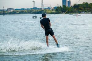 Rear view of wakeboarder sliding on water of city river holding on to towing rope photo