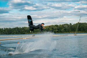 Confident male wakeboarder jumping over water surface on lake on summer day photo