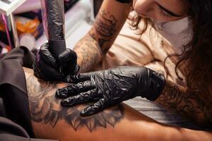 Professional tattooist creating black and white flower design on female thigh photo