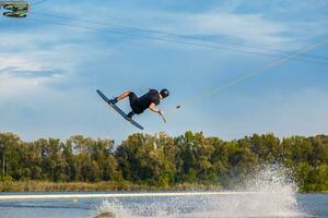 joven hombre hábilmente haciendo trucos en wakeboard en soleado día foto