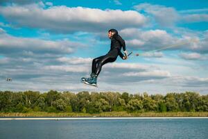 Man practicing technique of jumping over water with rotation during wakeboarding training photo