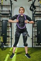 Beautiful blonde woman wearing in sensors and belts, fastens with velcro is practicing EMS fitness in a gym, building up muscles with espander. photo