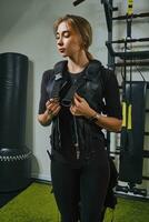 Beautiful blonde woman wearing in sensors and belts, fastens with velcro is practicing EMS fitness in a gym. Modern kind of sport. photo