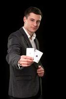 joven caucásico hombre vistiendo traje participación dos ases en su mano en negro antecedentes. juego concepto. casino foto