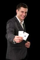 Young caucasian man wearing suit holding two aces in his hand on black background. Gambling concept. Casino photo