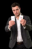 joven caucásico hombre vistiendo traje participación dos ases en su manos en negro antecedentes. juego concepto. casino foto