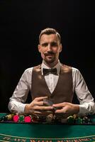 Portrait of a croupier is holding playing cards, gambling chips on table. Black background photo