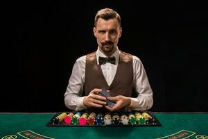 Portrait of a croupier is holding playing cards, gambling chips on table. Black background photo