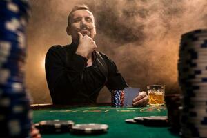 Handsome bearded man drinking whisky while playing poker photo