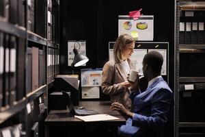 Managers checking accountancy report, working late at night at administrative record in corporate depository. Diverse businesspeople discussing bookkeeping documents in storage room. photo