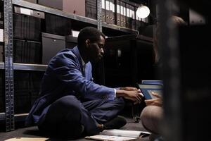 Corporate employees working overhours in storage room, analyzing administrative report discussing bureaucracy record. Bookkeepers examining management documents, organizing accountancy files. photo