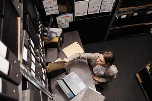 Top view of police officer typing criminal case report on laptop computer, analyzing crime scene evidence in arhive room. Private detective working overtime at federal investigation photo