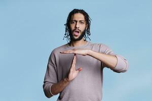 Arab man making time out gesture with hands and looking at camera portrait. Handsome young person showing interruption sign with arms, taking break from communication concept photo