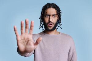 Serious arab man showing stop gesture with arm, looking at camera and talking. Young person making prohibition and rejection sign with confident facial expression portrat photo