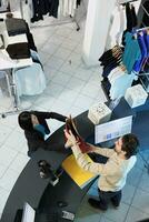 asiático mujer tomando papel compras bolso desde cajero a revisa escritorio mientras compras en ropa Tienda parte superior vista. Departamento centro comercial Moda boutique cliente haciendo compra a efectivo Registrarse foto