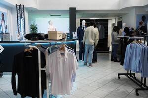 ropa Tienda cliente y asistente examinando formal traje en maniquí. Moda sala de exposición cliente consiguiendo recomendación desde asistente mientras compras para de moda atuendo foto