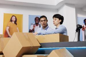 Diverse employees working at customers orders, preparing packages for delivery in modern boutique. Workers putting fashionable clothes in carton boxes, discussing shipping detalis at counter desk photo