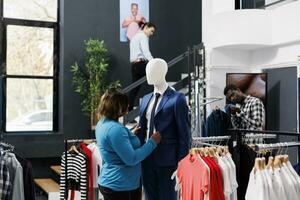 alegre mujer mirando a formal atar, analizando material en ropa almacenar. africano americano cliente compras para de moda casual tener puesto, moderno boutique lleno con de moda mercancías foto