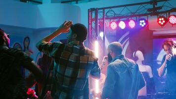 Young persons dancing on disco music, having fun with spotlights and dance moves at discotheque. Cheerful people enjoying social gathering with friends and performance show on stage. Tripod shot. photo