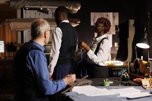 African american gentleman getting measurements taken by professional suitmakers in dark studio workspace. Masterful tailors looking for ideal client proportions for upcoming custom made suit photo