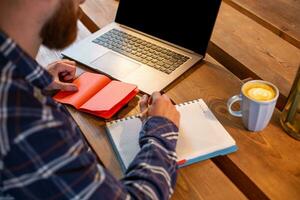 Cropped image of casual business man or freelancer planning his work on notebook, working on laptop computer with smart phone, cup of coffee on table at coffee shop or home office. photo