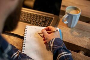 Cropped image of casual business man or freelancer planning his work on notebook, working on laptop computer with smart phone, cup of coffee on table at coffee shop or home office. photo