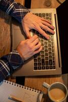 Young man drinking coffee in cafe and using laptop. Man's hands using laptop during coffee break photo