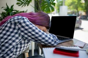 Young woman lying on her arms on the table in cafe in front of laptop with cup of coffee, sleepy. photo