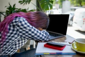 Young woman lying on her arms on the table in cafe in front of laptop with cup of coffee, sleepy. photo