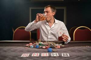 Handsome emotional man is playing poker sitting at the table in casino. photo