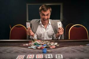 Handsome emotional man is playing poker sitting at the table in casino. photo