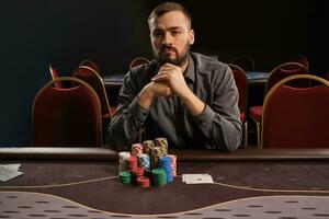 hermoso barbado hombre es jugando póker sentado a el mesa en casino. foto