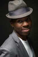 Portrait of attractive young black male studio with hat cheesy smile on dark background photo