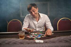 Handsome emotional man is playing poker sitting at the table in casino. photo