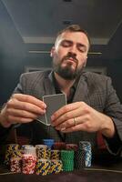 Handsome bearded man is playing poker sitting at the table in casino. photo