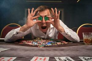 Handsome emotional man is playing poker sitting at the table in casino. photo