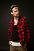 Handsome trendy young guy at the studio on black background. He wears beard and a plaid shirt photo