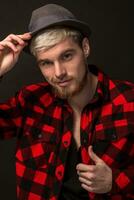 Handsome trendy young guy at the studio on black background. He wears beard and a plaid shirt photo