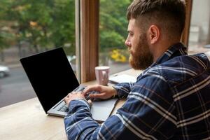 Young man chatting via net-book during work break in coffee shop, male sitting in front open laptop computer with blank copy space screen. photo