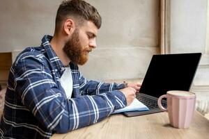 Young man chatting via net-book during work break in coffee shop, male sitting in front open laptop computer with blank copy space screen. photo